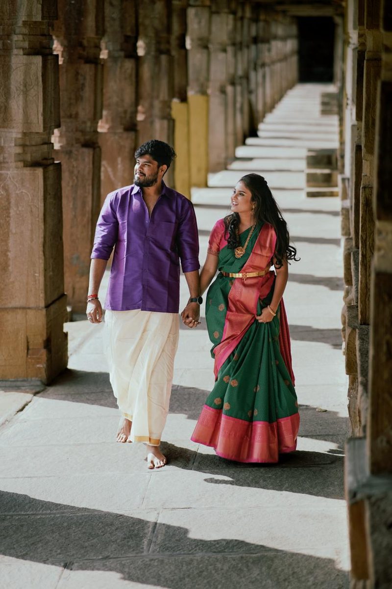 Couple walking hand in hand — veshti and green Kanjivaram at heritage steps